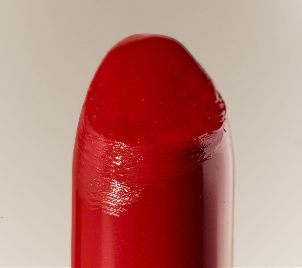 A close-up of a glossy red lipstick bullet against a light beige background.